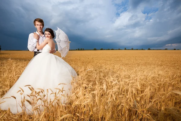 Young bride and groom in fantastic wheat field and dramatic sky
