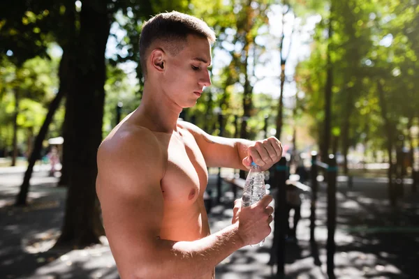 Athletic sport man drinking water from a bottle. Outdoor fitness.