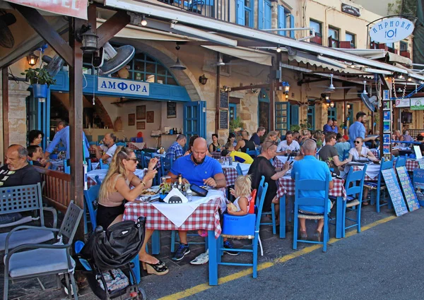 People sit in sidewalk street cafe in Chania waterfront, Crete,