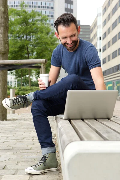 Relaxed man sitting outdoors and working on laptop