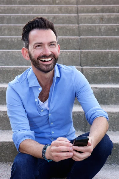 Smiling mature guy sitting outdoors with mobile phone