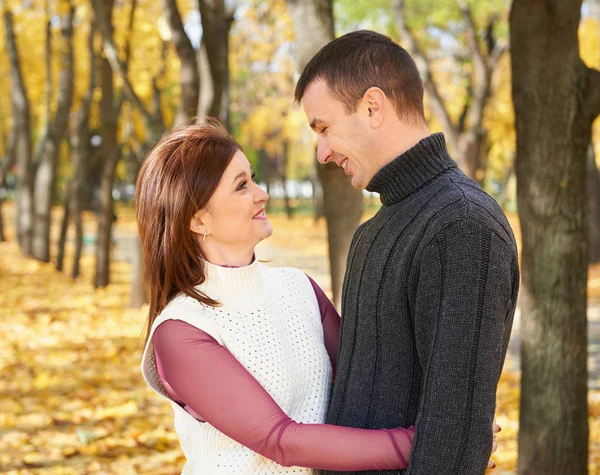 Happy adult couple embrace in autumn city park, trees with yellow leaves, bright sun and happy emotions, tenderness and feelings