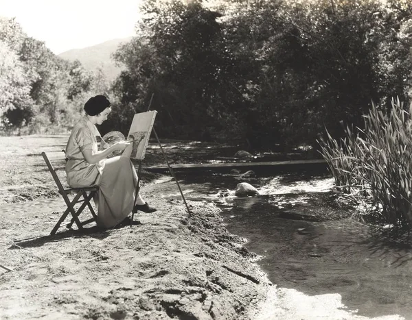 Woman painting by river