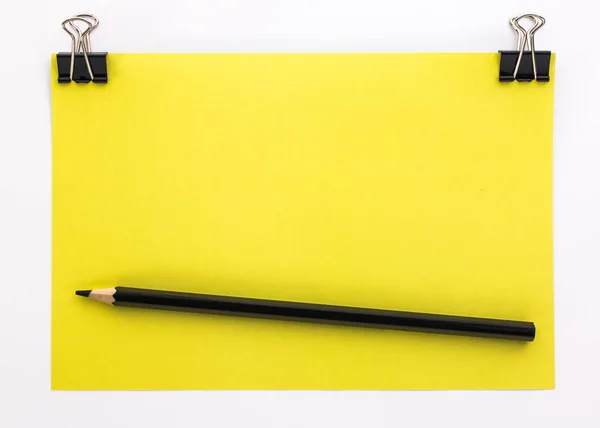 Yellow piece of paper with black paper clips and black pencil