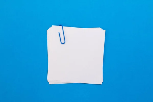 White sheet of paper with blue paper clip on a blue background