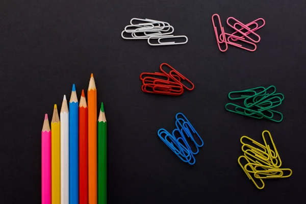 Colored pencils and paper clips on a black background