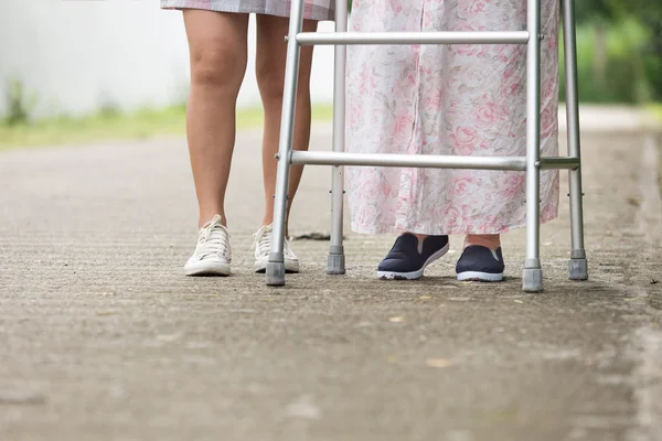 Senior woman using a walker with caregiver on street.