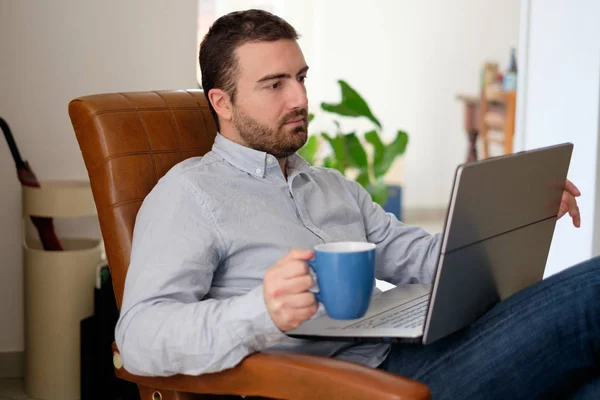 Man working at home using his laptop and drinking coffee