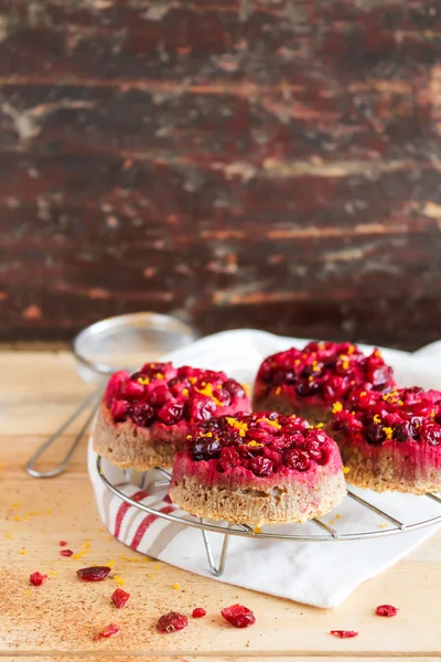 Gluten free homemade cakes with fresh cranberry, whipped cream, lemon zest and cinnamon on top on a wooden table and on the cooling rack, selective focus