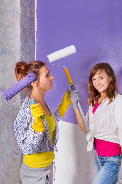 Young beautiful women paints white wall with purple paint roller