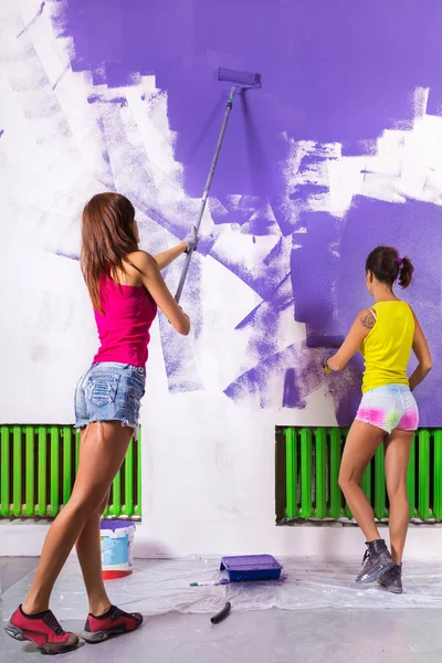 Women paints white wall with purple paint roller