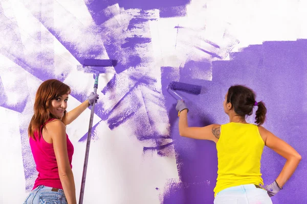 Women paints white wall with purple paint roller