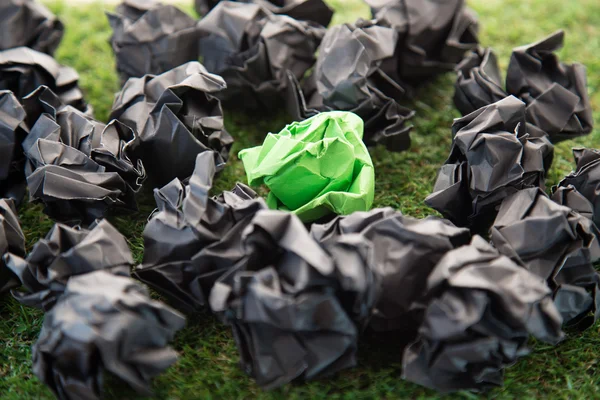 Green crumped paper between black paper balls on  grass field.jp
