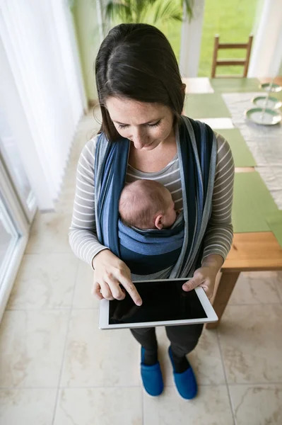 Mother with son in sling, holding tablet