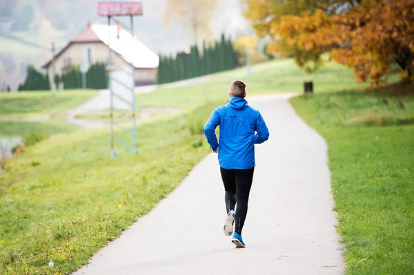 Athlete at the lake running on concrete path, rear view.