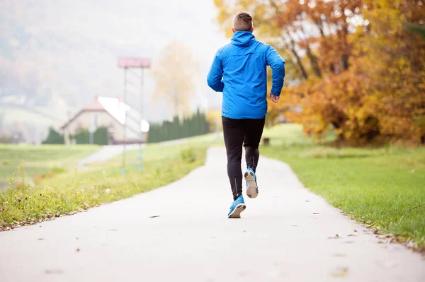 Athlete at the lake running on concrete path, rear view.