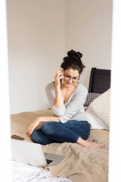 Woman sitting on bed, making phone call. Home office.