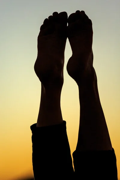 Silhouette legs of meditating woman in front of the red sinking sun on desert