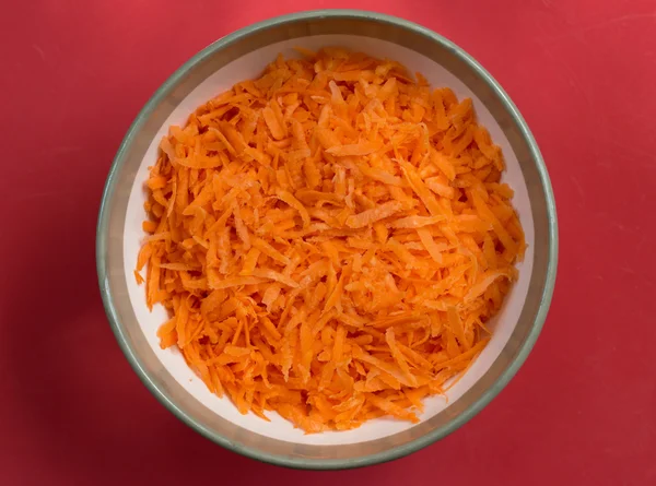 Close-up view of grated carrot is in round bowl.