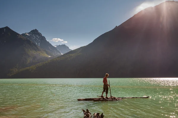 Man on wooden raft tries to cross the lake in high mountains