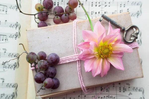 Old book with vintage key, grapes and pink flower on playing notes