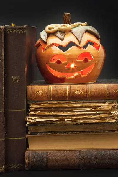 Pumpkin lantern for Halloween and the old witch books. Head carved from a pumpkin on Halloween. Pumpkin tradition. The book of spells, magical book. Textbooks for witches.