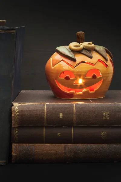 Pumpkin lantern for Halloween and the old witch books. Head carved from a pumpkin on Halloween. Pumpkin tradition. The book of spells, magical book. Textbooks for witches.