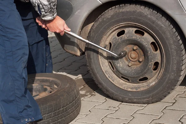 Man is changing winter tire with wheel wrench. Preparing the car for the winter. Repairing punctured tires.
