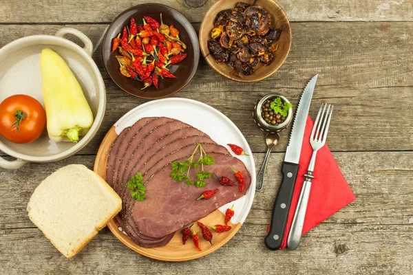 Cold roast beef on a wooden table. Delicacy of beef. Preparing cold refreshments. Traditional meal. Beef roast beef with green pepper and chili peppers and vegetables.