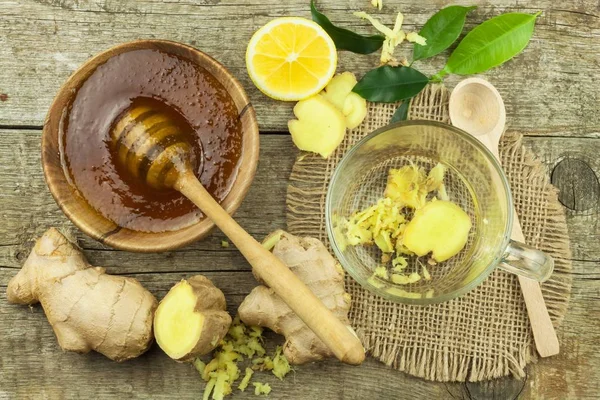 Preparing ginger tea against influenza. Traditional treatment for colds. Ginger, lemon and honey bowl on wooden table. Rustic wooden background. Home Pharmacy.