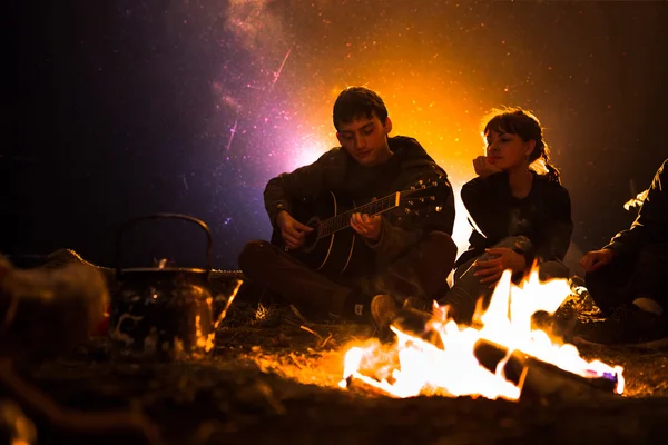 Man plays guitar and woman about the fire on the background of the starry sky