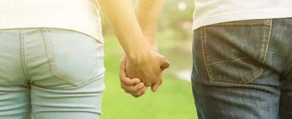 Back view of young casual couple holding hands while walking in