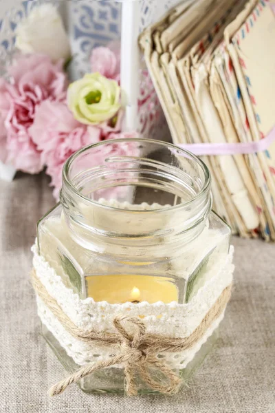 Glass jar with candle inside decorated with lace and string.