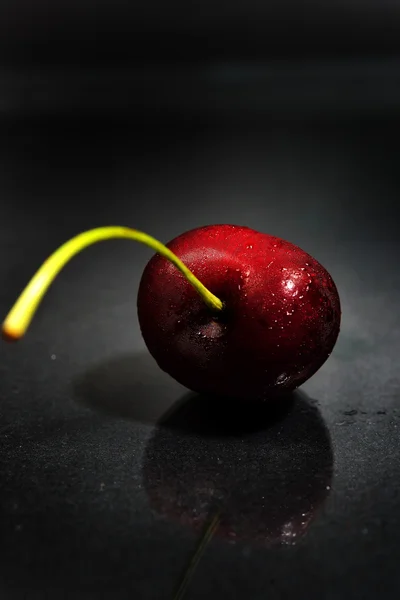 Macro photo of red cherry with water drops on black background.