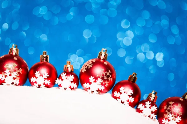 Christmas red balls in snow on blue glitter background