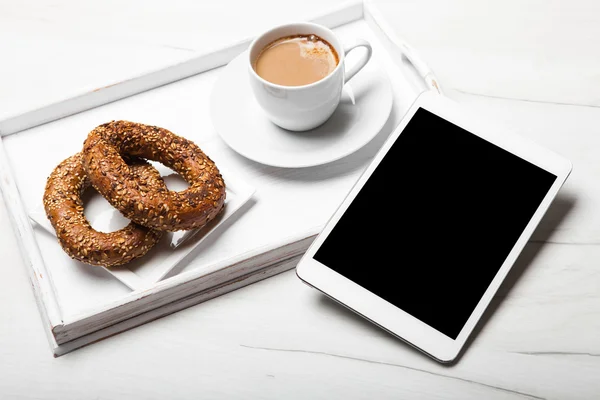 Digital tablet, breakfast and cup of coffee on old wooden desk.