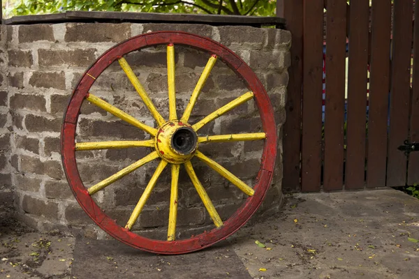 Old wagon wheel with metal rim leaning on a stone wall
