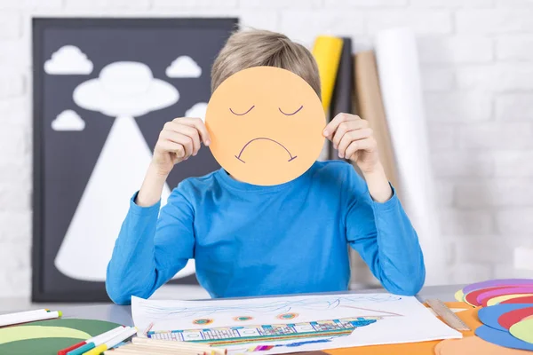 Boy is holding a paper mask with sad face