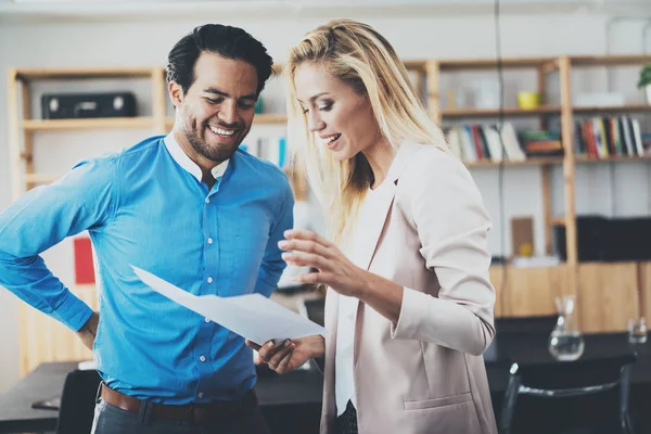 Two young professionals making a great business discussion in modern office.Successful confident hispanic businessman talking with woman partner. Horizontal, blurred background.