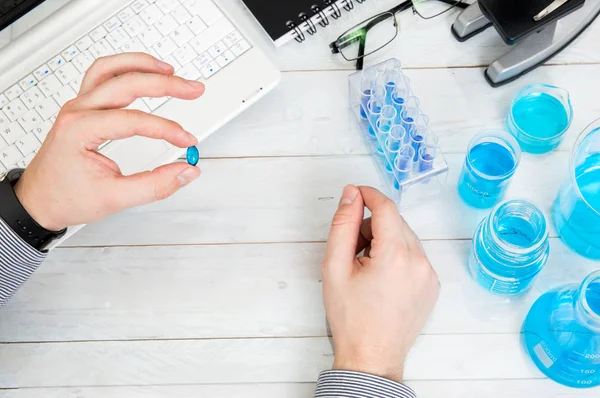 Man holds blue pill above desk with laboratory tools