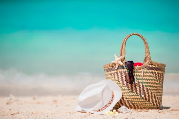 Straw bag, fist star, headphones, hat and sunglasses on white beach