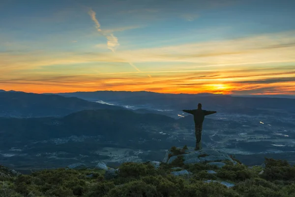 Man with open arms on top of the mountain at sunrise