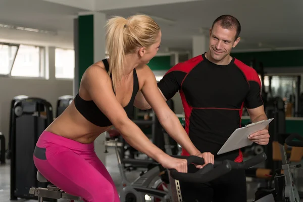 Woman Train Bicycle On Machine With Personal Trainer