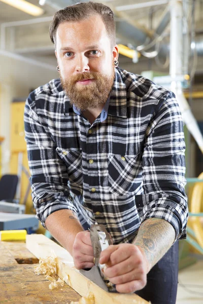 Carpenter work with plane on wood plank in workshop