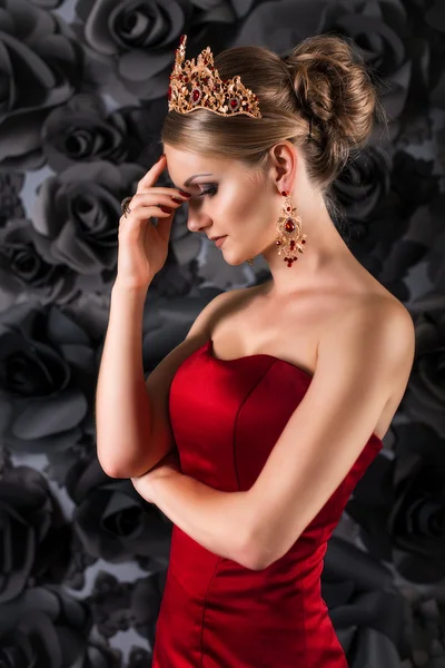 Beautiful young blonde woman in red long dress with fluffy skirt on a black background. queen, golden crown on the head, golden curls, passionate girl in red