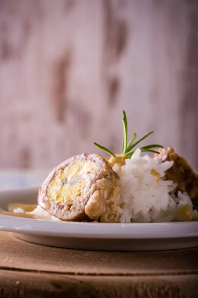 Meat rolls filled by eggs and cheese with rice on plate and wooden board