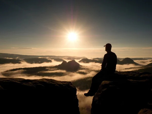 Moment of loneliness. Man with cap sit on mountain and watch to fog