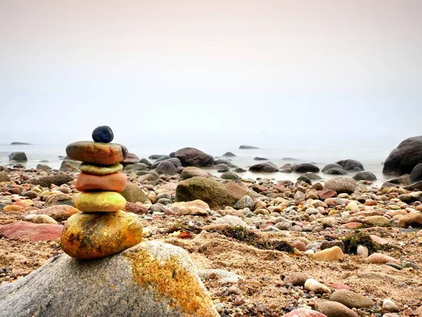 Balanced stone pyramid on sea shore, waves in background. Colorful flat stones