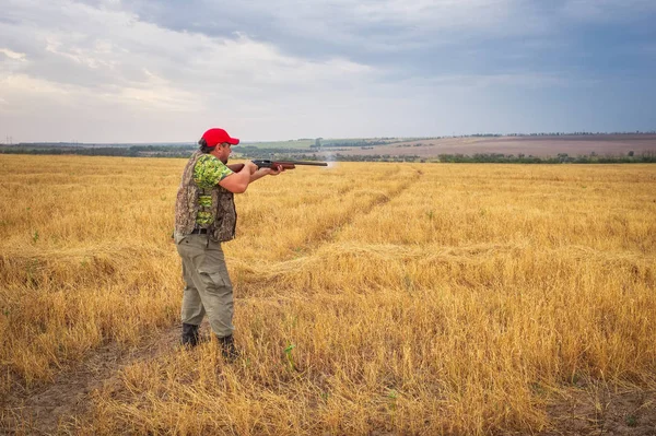 Hunter with a gun in the field aiming at the target and shoot