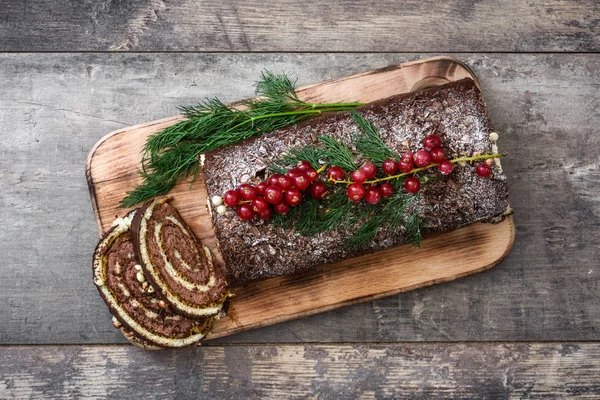 Chocolate yule log christmas cake with red currant on wooden background